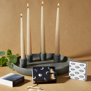 Gold star, moon phases, and evil eye match boxes with tapered candles on a tan backdrop.