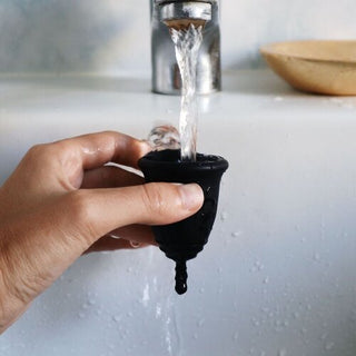 rinsing a black menstrual cup under running faucet